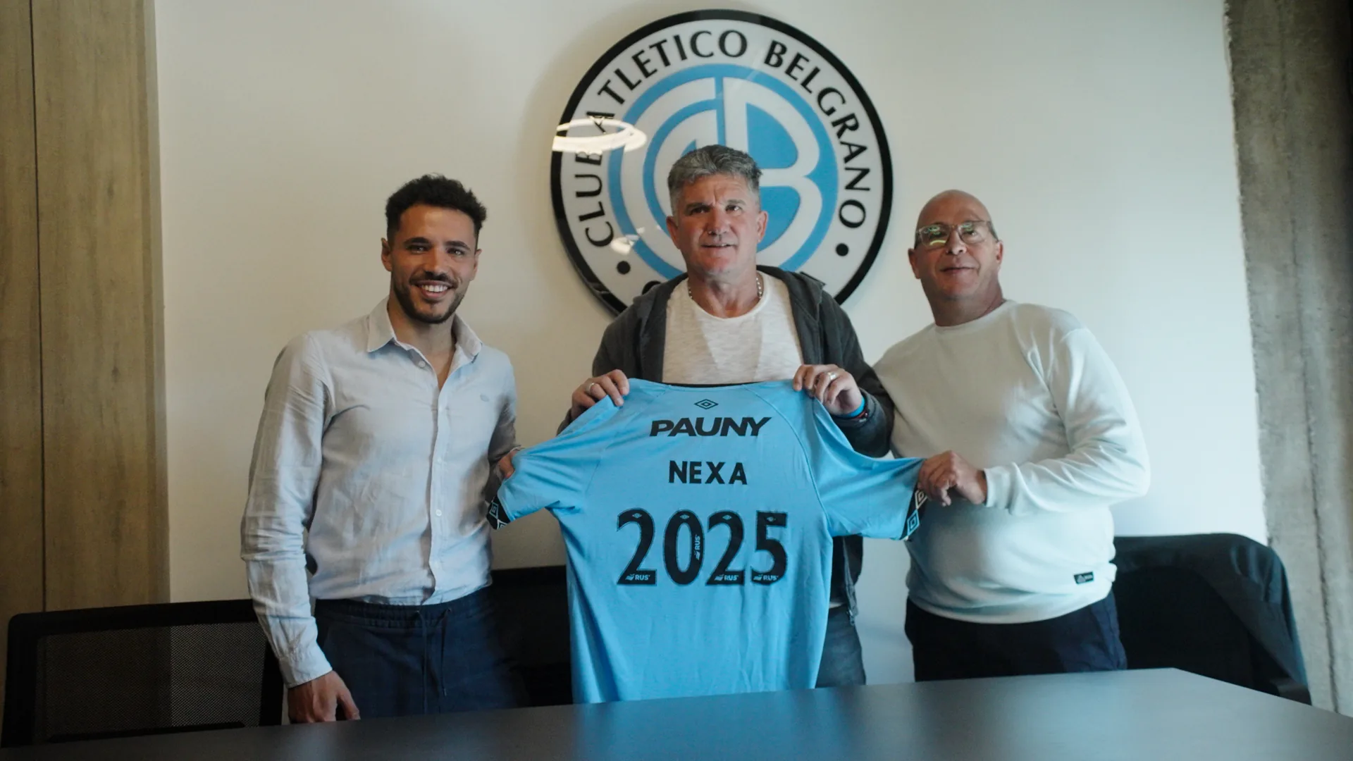 Luifa Artime sostiene la camiseta de Belgrano con el sponsor Nexa 2025, en la firma del contrato