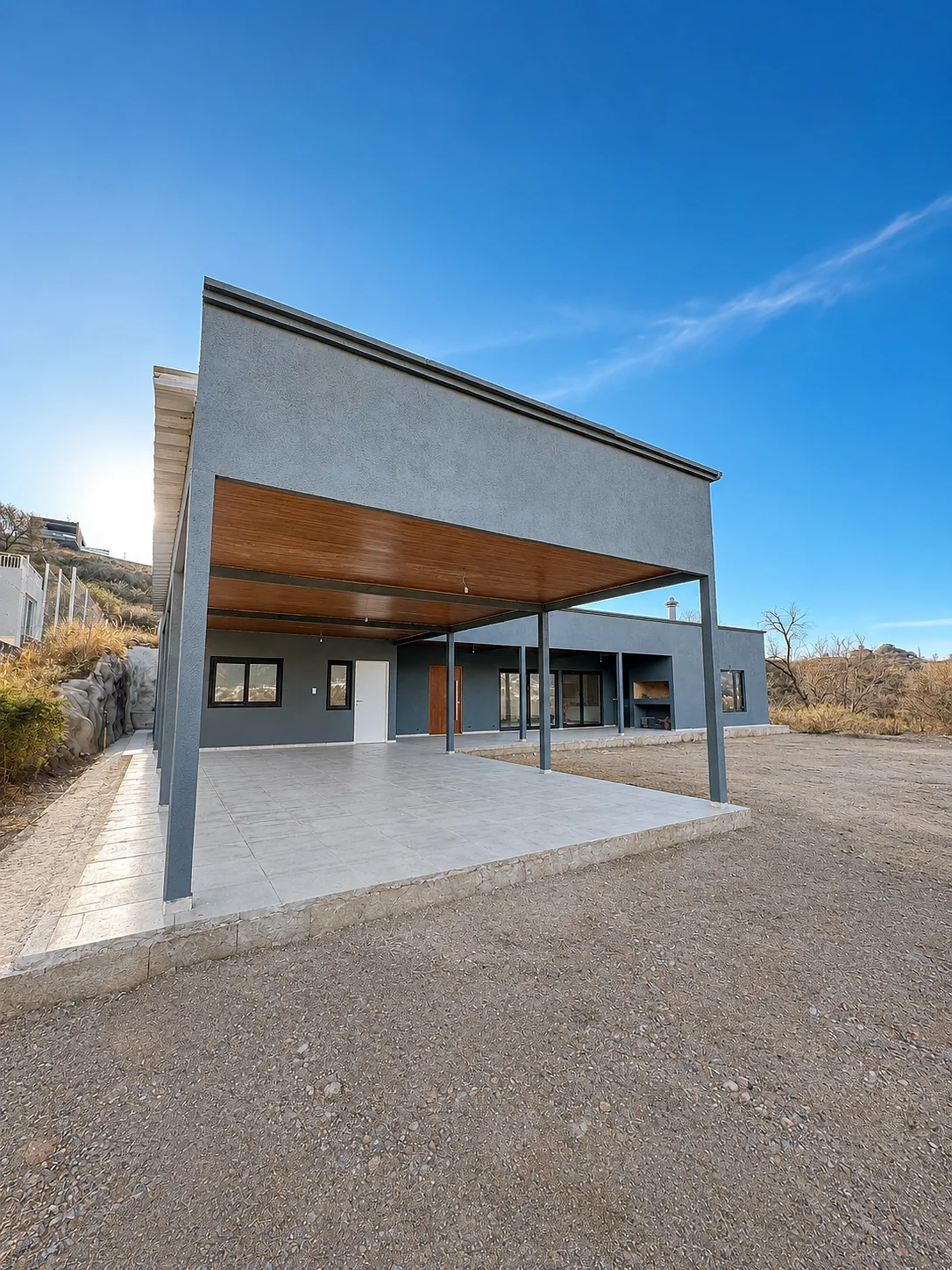 Altos de Carlos Paz — La galería vista desde afuera: alero con cielorraso color madera, columnas finas y el frente de la casa detrás