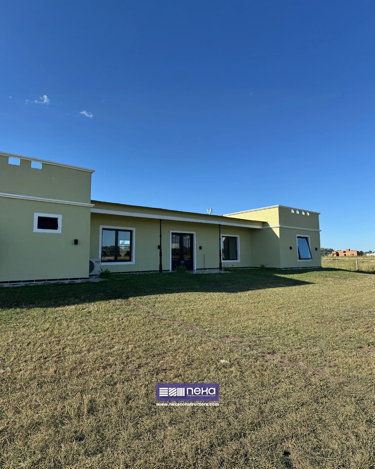 Chacras de San Andrés · Casa 2 — La casa entera desde el parque: una planta, muros verde claro y carpinterías negras
