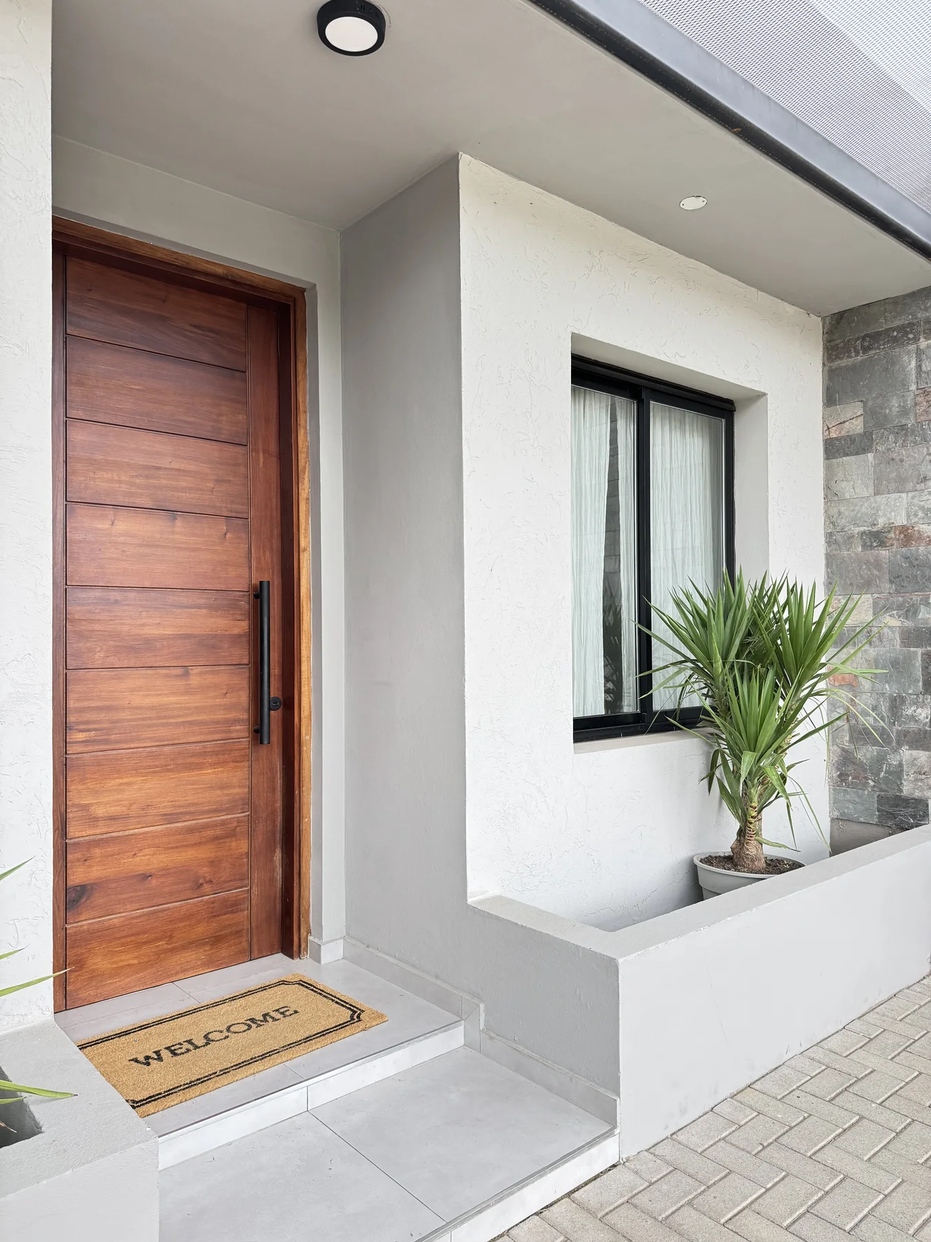 Docta — El ingreso: la puerta de madera, el cantero con una planta y la pared revestida en piedra