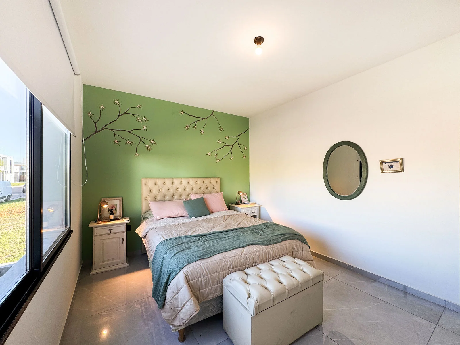 Docta — Un dormitorio con la pared verde pintada con ramas, la cama y una ventana al costado