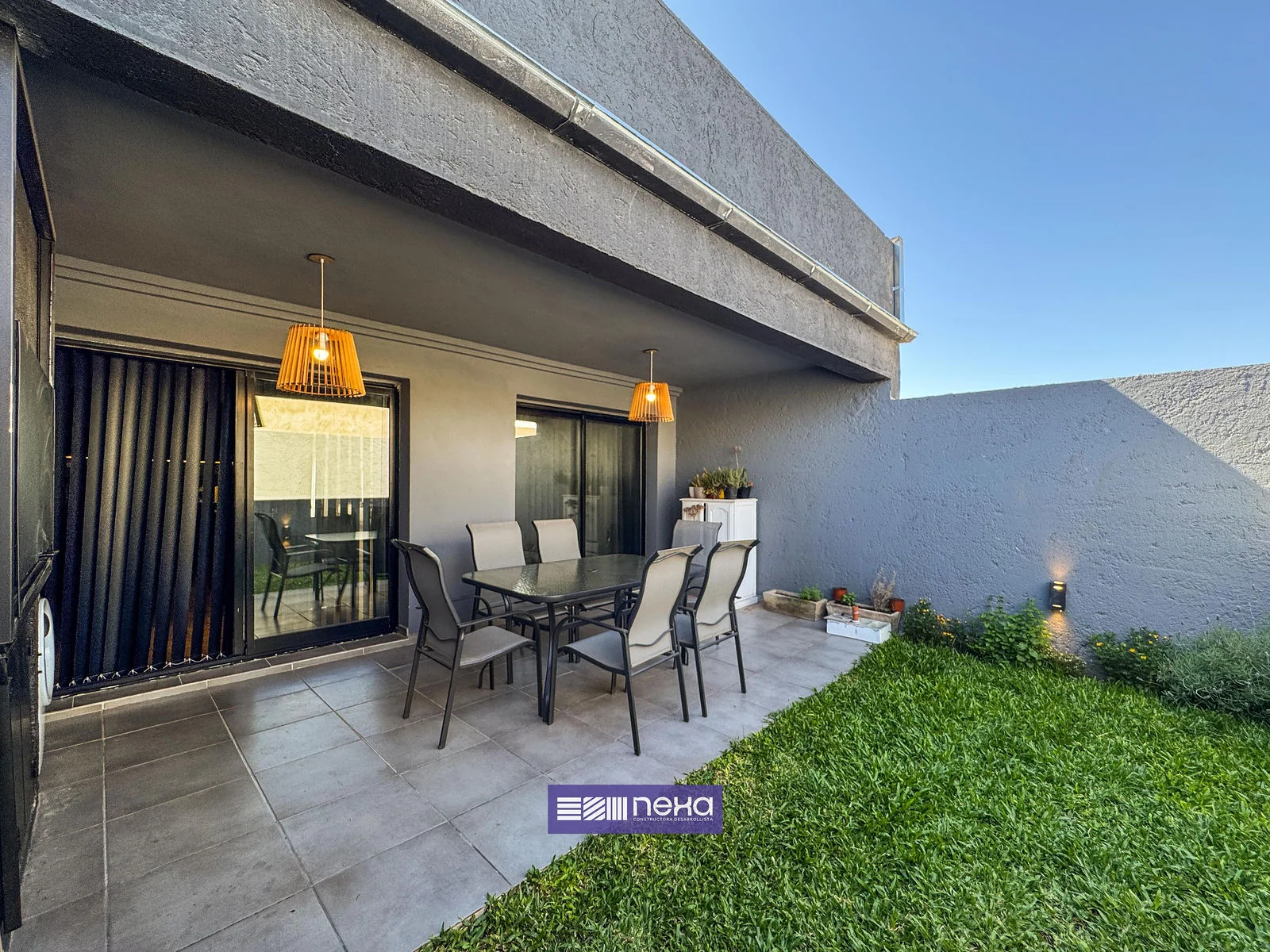 Rincones de Manantiales — Galería techada con mesa y lámparas colgantes, frente al patio de pasto