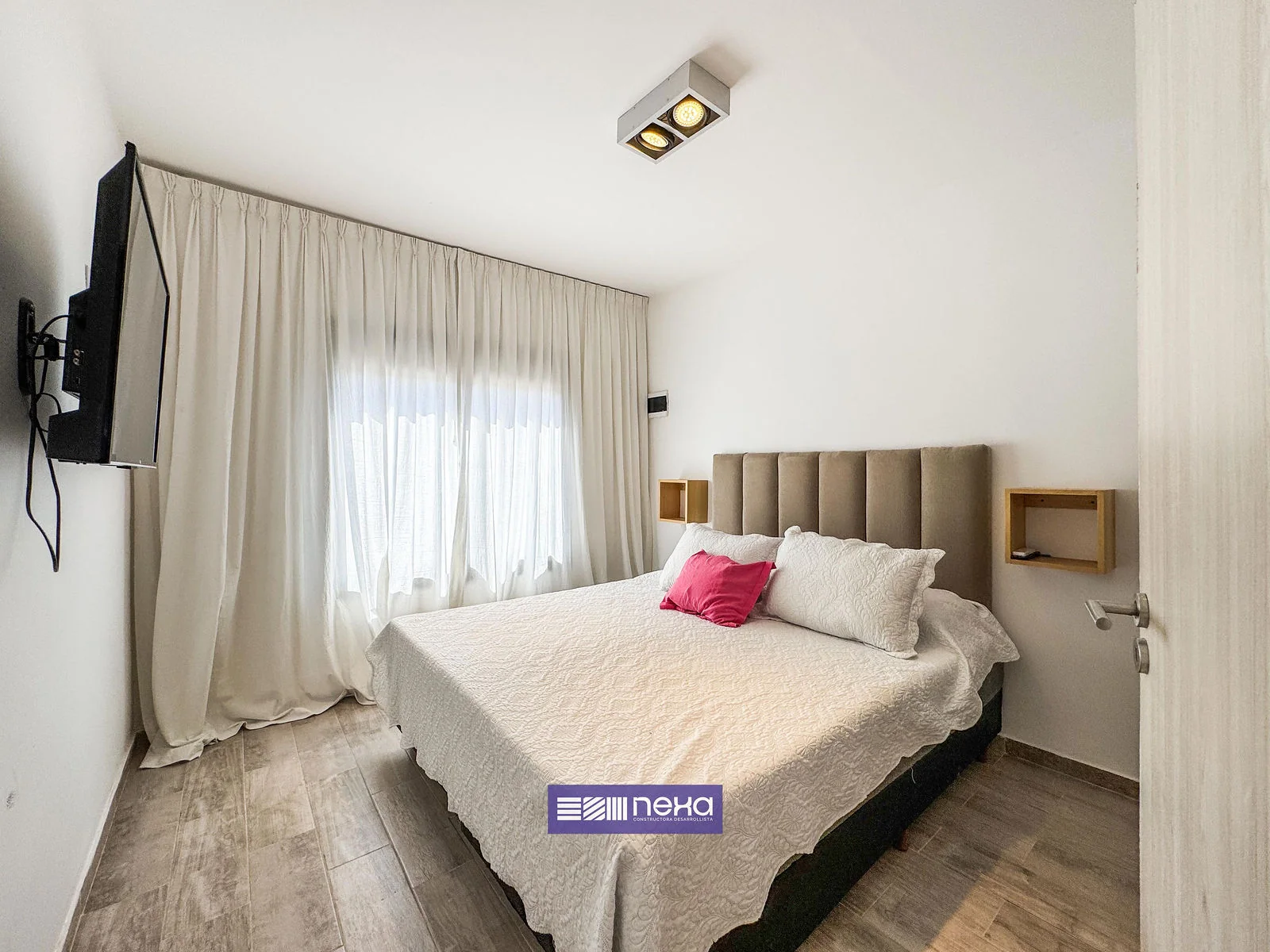 Rincones de Manantiales — Dormitorio con respaldo tapizado, ventana con cortinas y tele en la pared