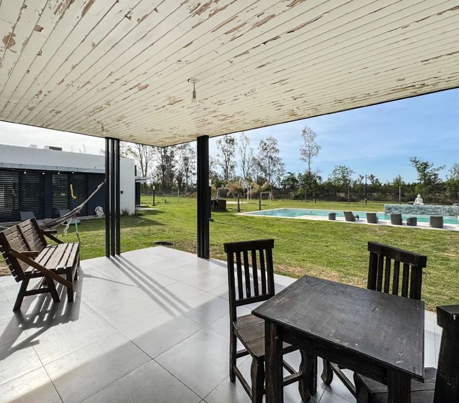 La Melinca Country Golf — Bajo la galería: mesa y sillas de madera mirando al parque y la pileta