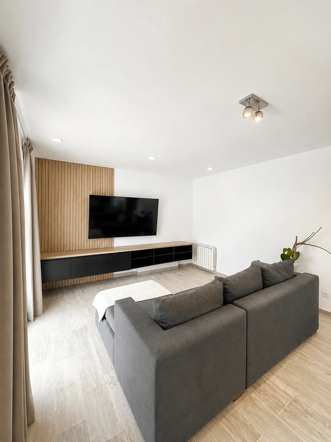Tejas Cuatro — Living con sillón gris y mueble de TV sobre una pared de listones de madera
