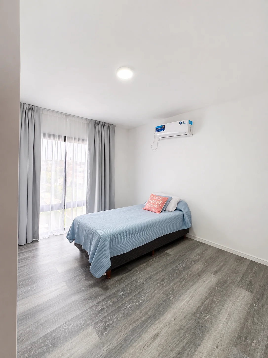 Tejas Cuatro — Dormitorio con cama de una plaza, cubrecama celeste y cortinas grises