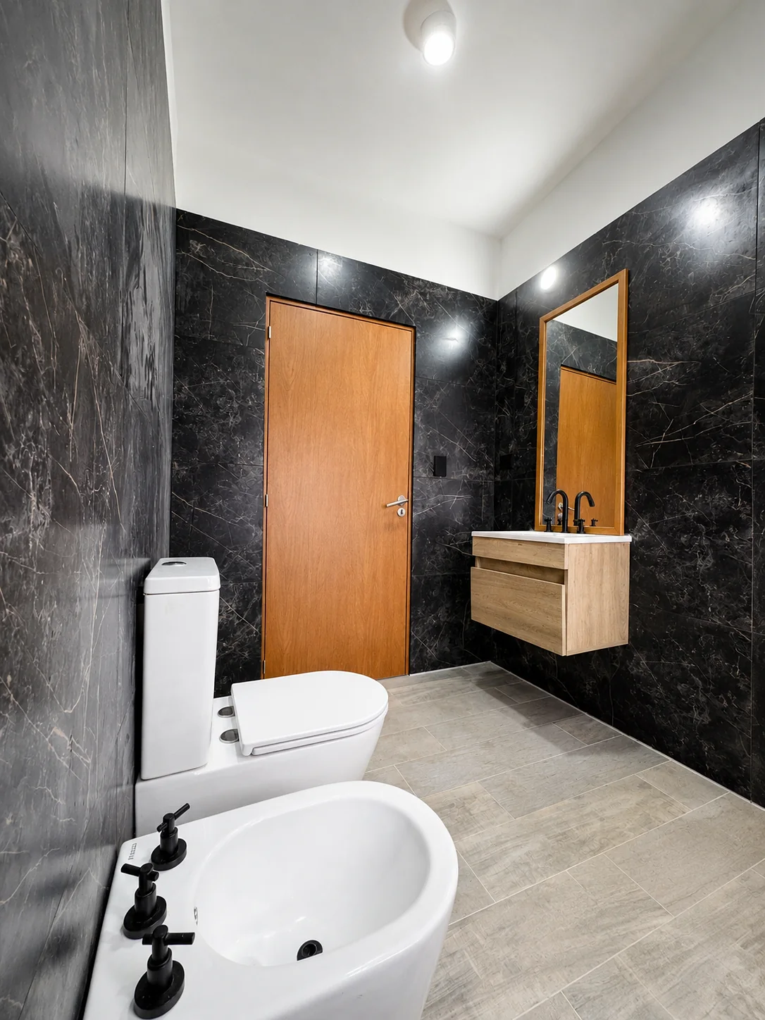 Tejas Cuatro — Baño en suite con revestimiento oscuro veteado: inodoro, bidé y vanitory de madera con espejo