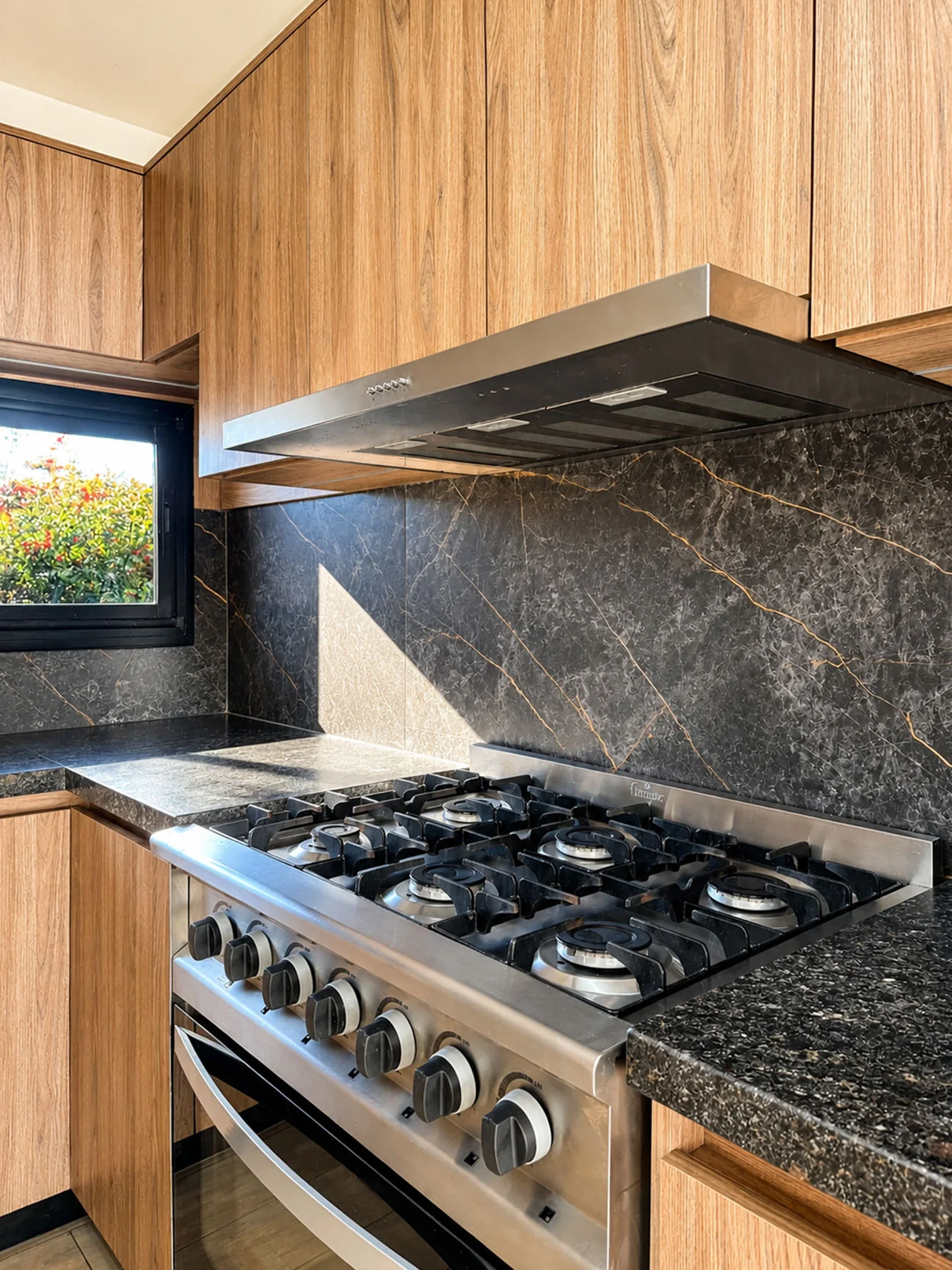 Villa Giardino — Cocina a gas y campana de acero sobre el revestimiento de piedra oscura