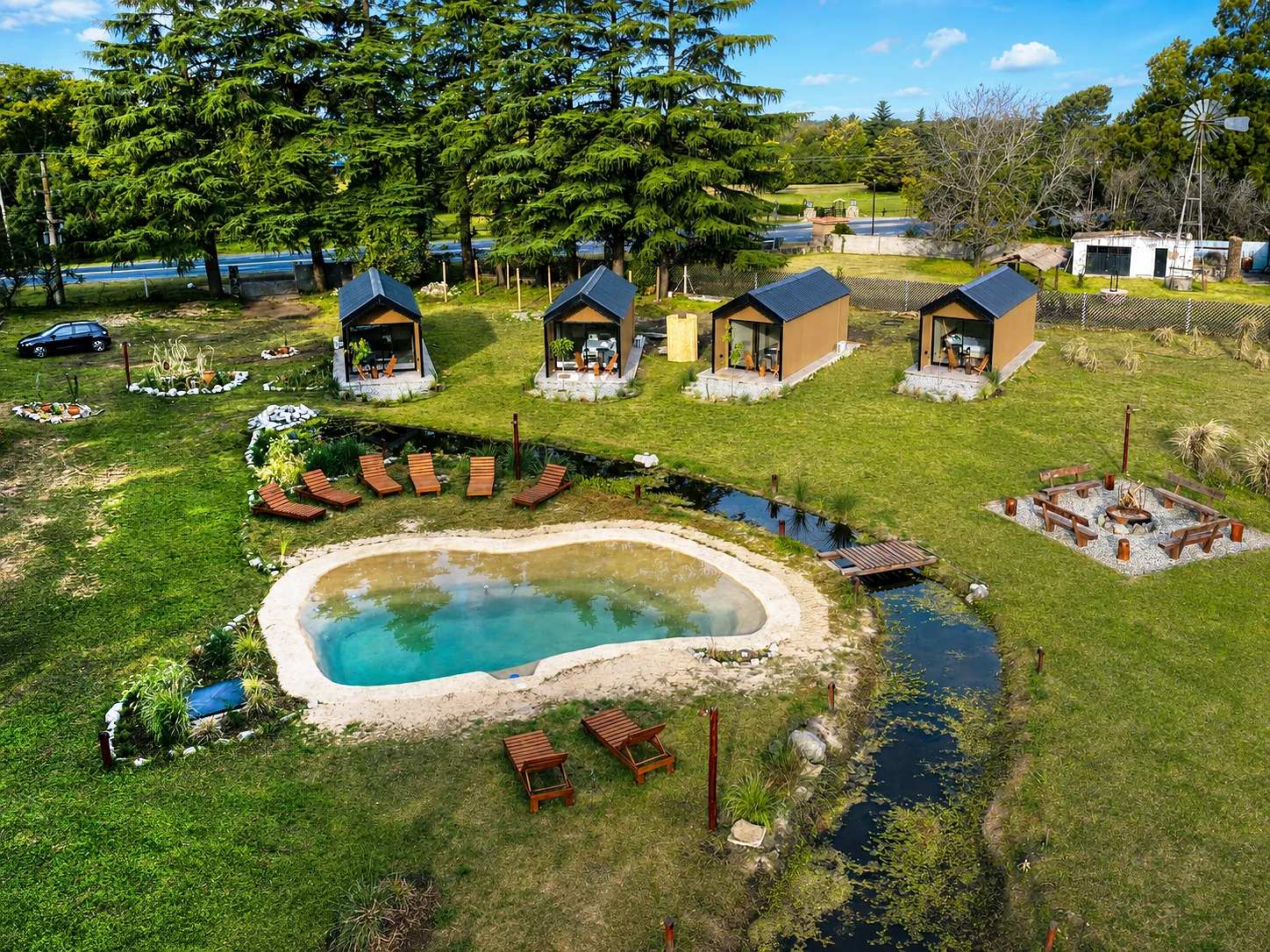 Villa Vadori · Suites Serranas — Vista aérea del complejo: las suites, la pileta, el arroyo con un puente de madera y el fogón