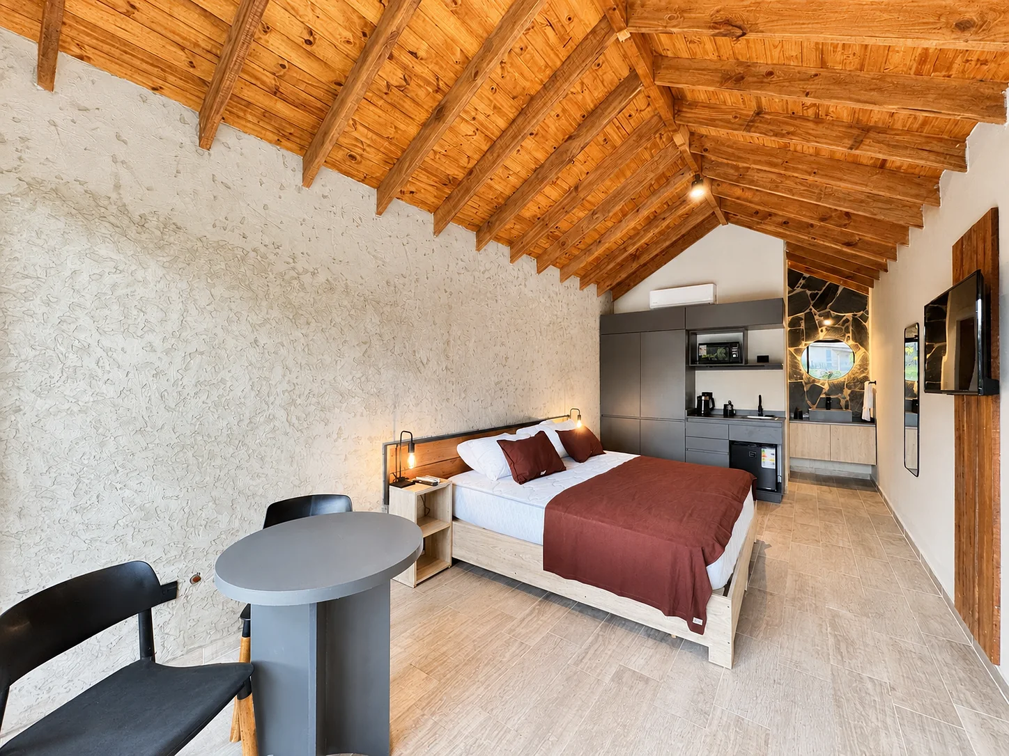 Villa Vadori · Suites Serranas — Interior de una suite: mesa, cama y kitchenette bajo el techo de madera a dos aguas